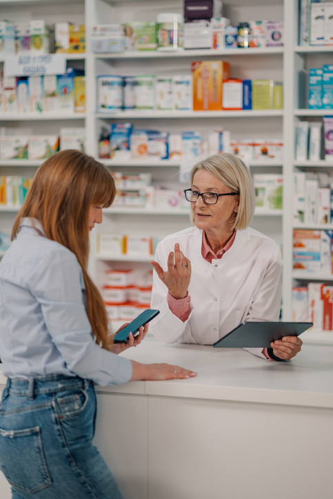 Senior druggist with tablet having consultations with client at drugstore pharmacy